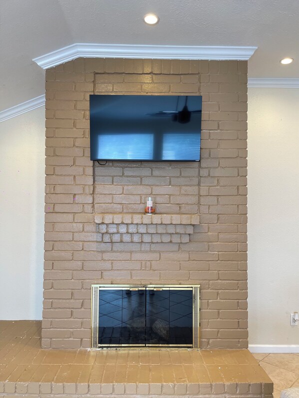 A flat-screen TV mounted on a brick wall above a fireplace with a glass door.