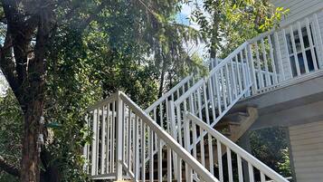 Un escalier en bois avec des rampes blanches mène à une terrasse, qui est entourée d’arbres et d’une clôture.