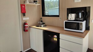 Une petite cuisine équipée d’un four à micro-ondes, d’un grille-pain et d’une machine à café. Un extincteur est fixé au mur, et une fenêtre offre une vue sur l’extérieur.