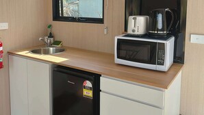 Eine kompakte Küche mit Geschirrspüler, Mikrowelle und Kaffeemaschine auf der Arbeitsfläche. Über der Spüle befindet sich ein Fenster, und eine Regalkonstruktion mit Geschirr und Küchenutensilien.