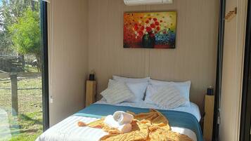 A bedroom with a bed, pillows, a painting, and a window.