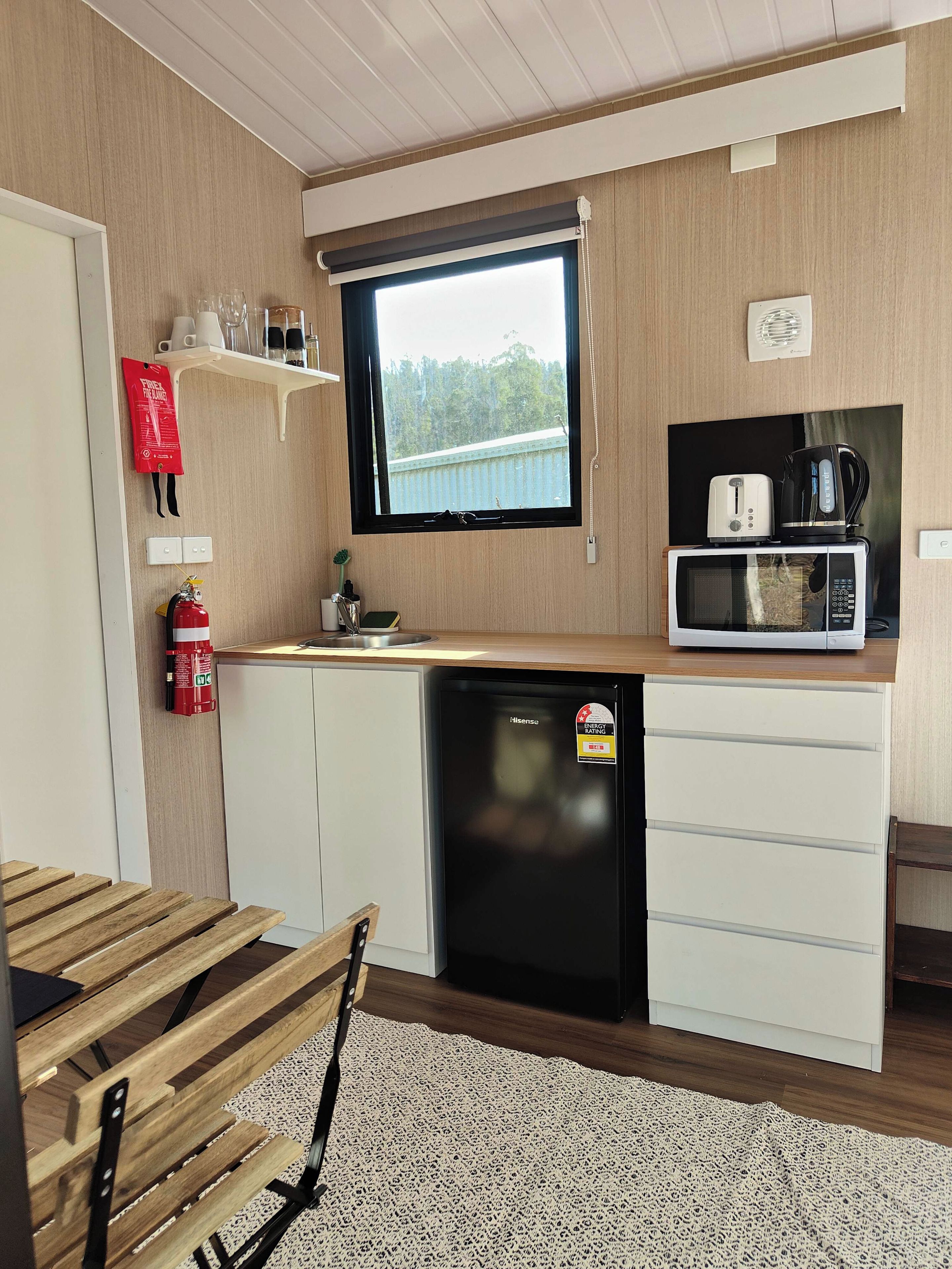 A compact kitchen with a microwave, toaster, and coffee maker on the countertop, a small sink, and a fire extinguisher mounted on the wall.