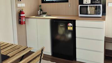 A compact kitchen with a microwave, toaster, and coffee maker on the countertop, a small sink, and a fire extinguisher mounted on the wall.
