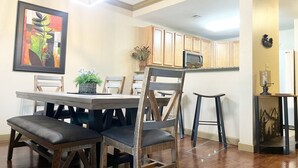 Un comedor con una mesa y sillas de madera, una lámpara colgante y una cocina al fondo.
