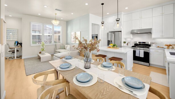 A modern kitchen with white cabinets, a dining area with a wooden table set for four, and a living area with a sofa and a coffee table. - Brand New Grand Luxury Designer Home in Irvine with Pool & Amenities (Irvine)