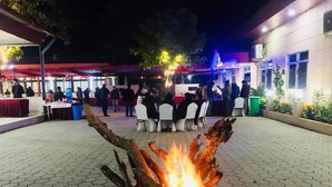 An outdoor event area with a central fire feature, tables, and chairs arranged for guests. - The Narayani Resort (Gaindakot)