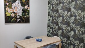 Zona pranzo con tavolo in legno, quattro sedie e una ciotola decorativa blu. Un quadro raffigura un leopardo tra fiori appeso al muro.