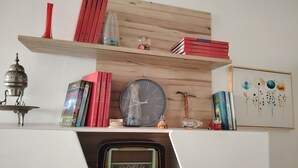 Una mensola con libri, un orologio, una radio e oggetti decorativi.