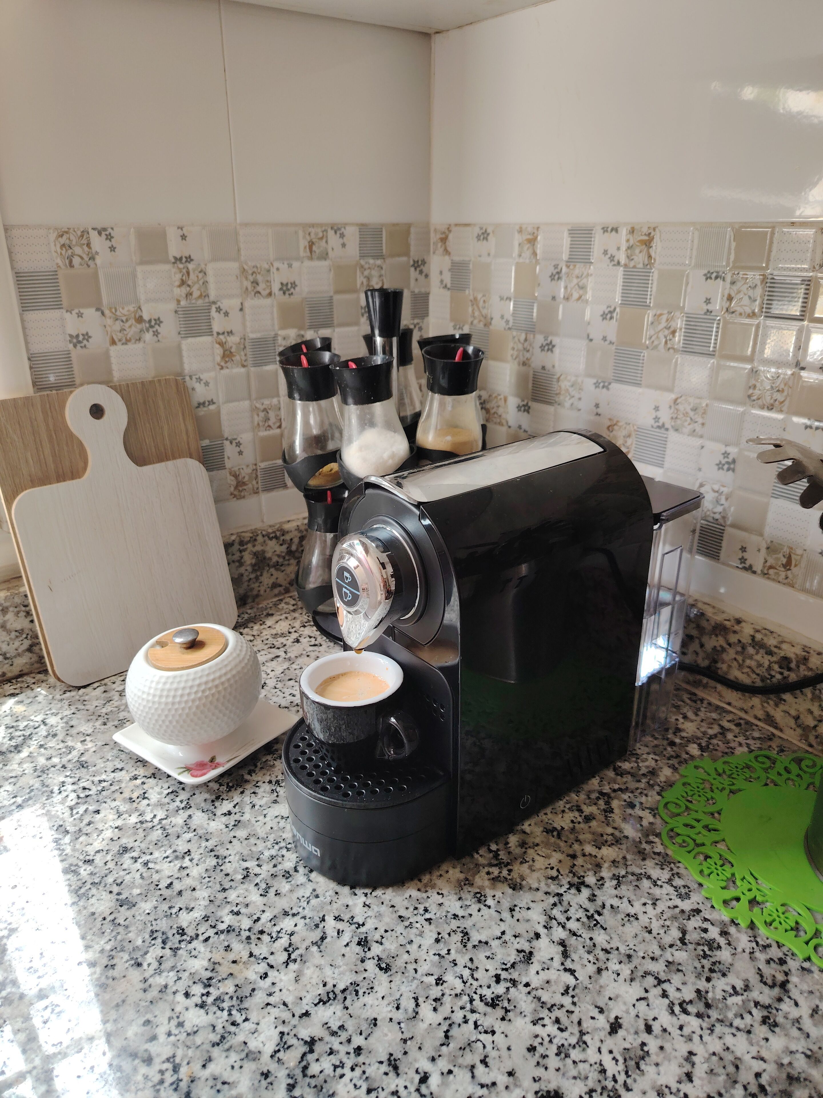 En kaffemaskine med en kop kaffe på et fad, en skærebræt og en kniv på bordet.