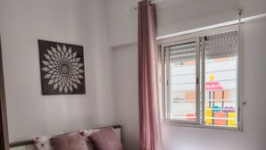 Una camera da letto con un letto, un comodino, una finestra con tende e un’opera d’arte appesa al muro.