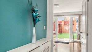 A hallway with a teal wall, a white console table with a vase, and a view into a backyard with a red fence and a car.