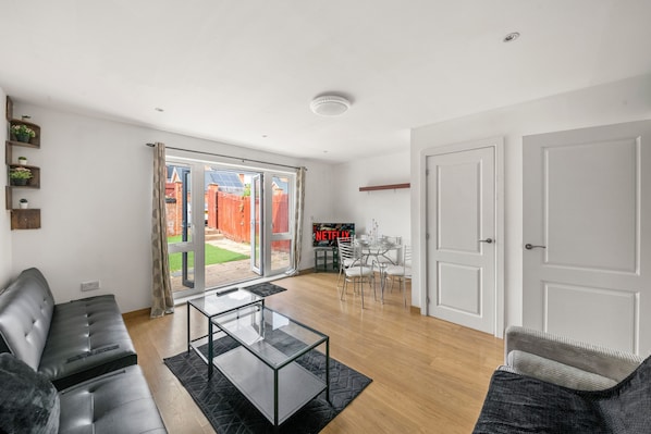 A modern living room with a glass coffee table, a sofa, and a dining area with chairs.