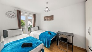 A bedroom with two beds, a desk, a chair, a clock, and a cityscape painting.