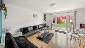 A modern living room with a grey sofa, a glass coffee table, and a view through a glass door to a garden.