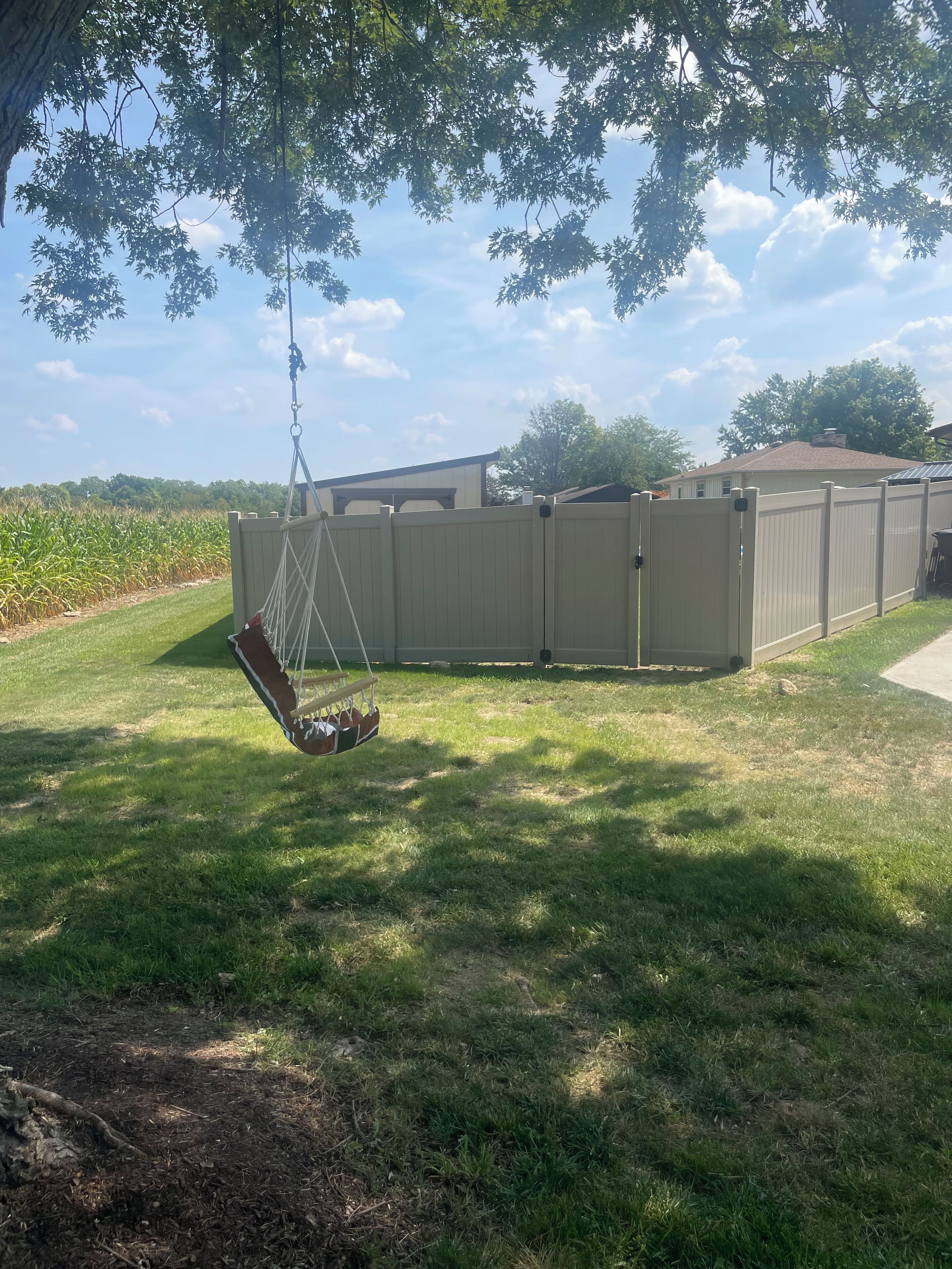 A backyard with a swing set, a fenced area, and a house in the background.