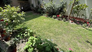 Hyvin hoidettu puutarha, jossa on monenlaisia kasveja ja kukkia, päällystetty alue ja tiilikattoinen rakennus.