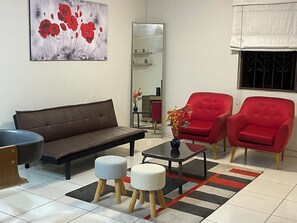 A modern living room with a brown sofa, two red armchairs, a coffee table, and a black vase with flowers. - Alojate.pe (Santiago de Surco)