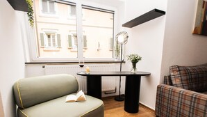 Een gezellige woonkamer met een groene bank, een geruite bank, een kleine tafel met een vaas en een raam met luiken.