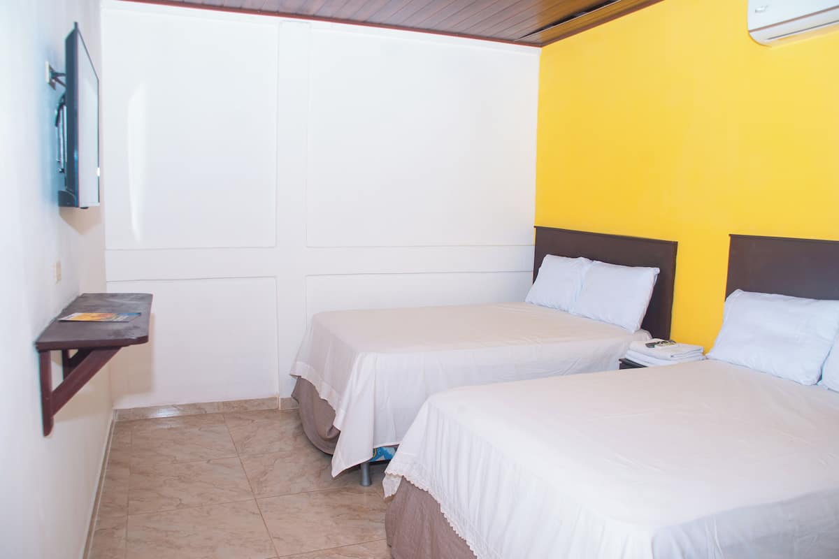 A hotel room with two beds, a small table, and a wall-mounted TV.