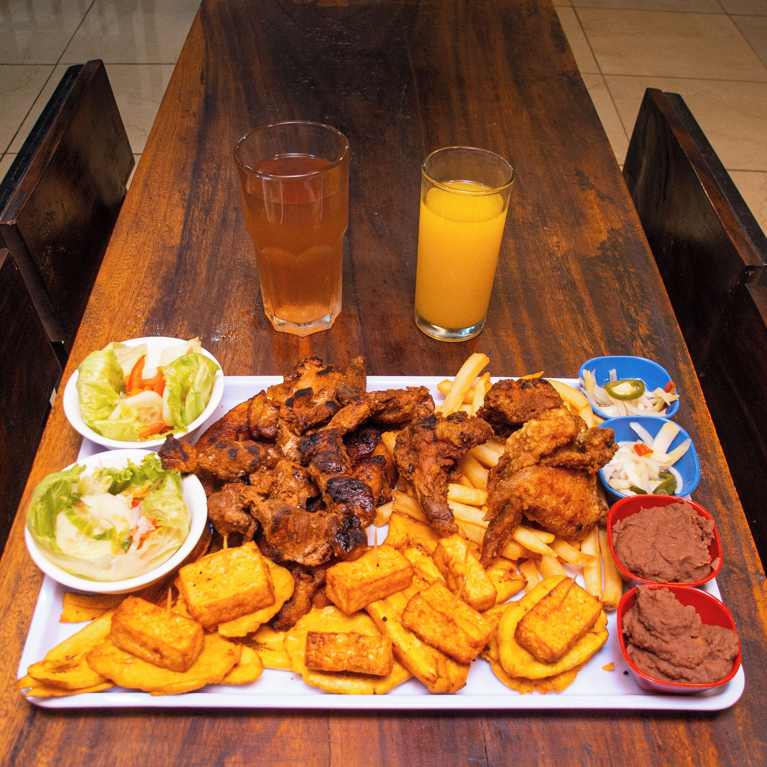 Un tavolo di legno con diversi cibi, tra cui pollo fritto, patatine fritte e una bevanda.