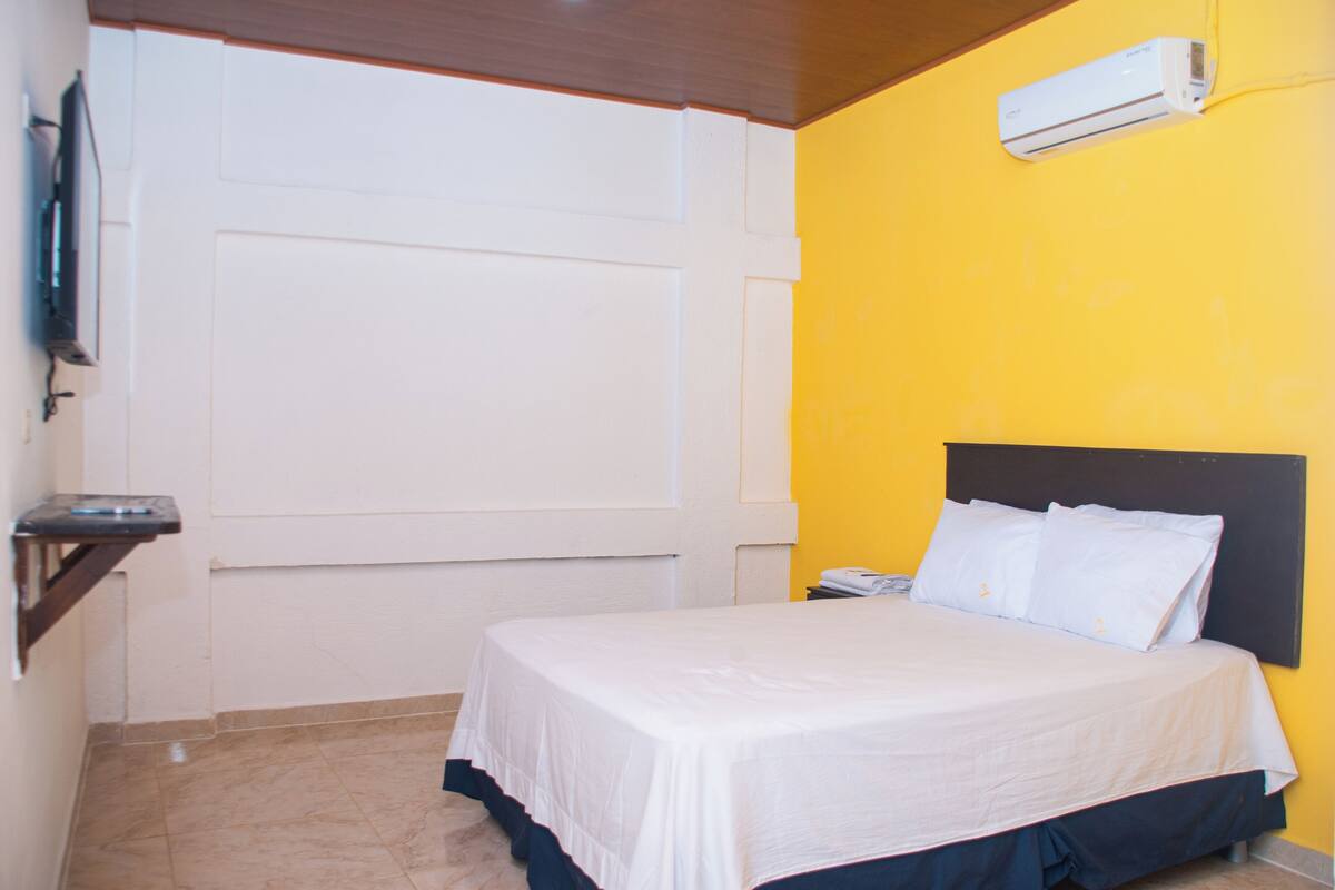 A hotel room with a bed, a nightstand, a wall-mounted air conditioner, and a door.