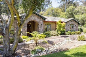 A stone house with an arched entrance, a tiled roof, and a well-maintained garden with various plants and a small pond. - Beautiful 4b 3+ba 30 Night minimum (Aptos)