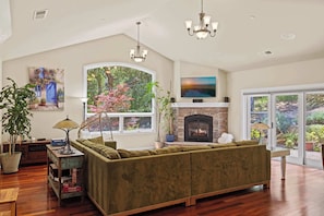 A spacious living room with a sectional sofa, a fireplace, large windows, and a chandelier. - Beautiful 4b 3+ba 30 Night minimum (Aptos)