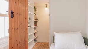 Un dormitorio con un armario de madera, estantes blancos, una cama con ropa de cama blanca y una planta colgante.