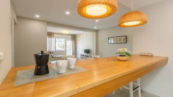 Una cocina moderna con encimera de madera, cafetera, tazas blancas y una lámpara colgante de fibras.