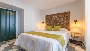 Een hotelkamer met een bed, een groene deur, een decoratief hoofdbord, twee nachtlampen en een nachtkastje.