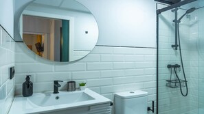 Een moderne badkamer met een wit wastafelmeubel, een ronde spiegel, een douchecabine met glazen wanden en een wit toilet.