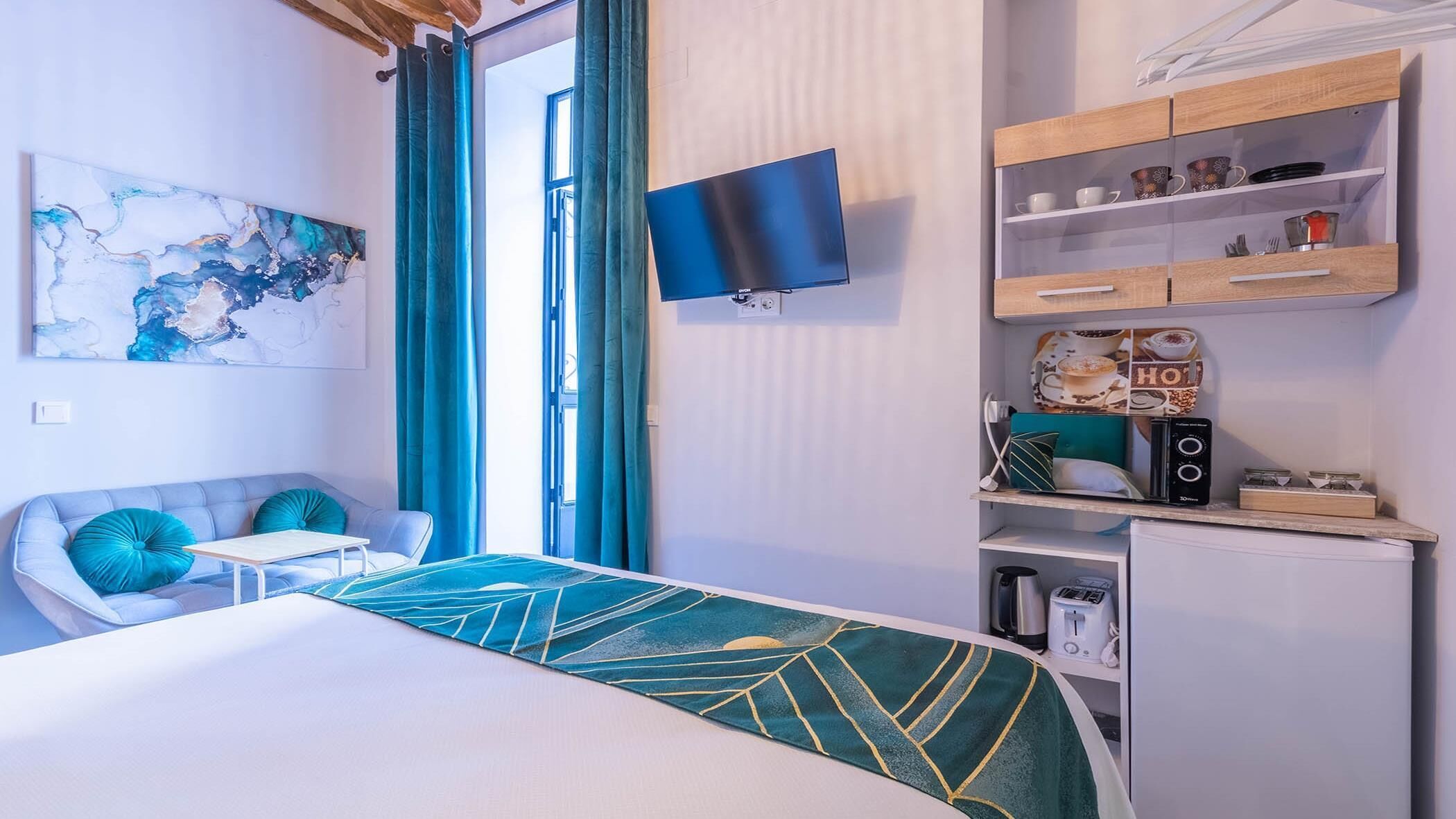 A modern room with a bed, a TV, a kitchenette, and a seating area with a view of the outdoors.
