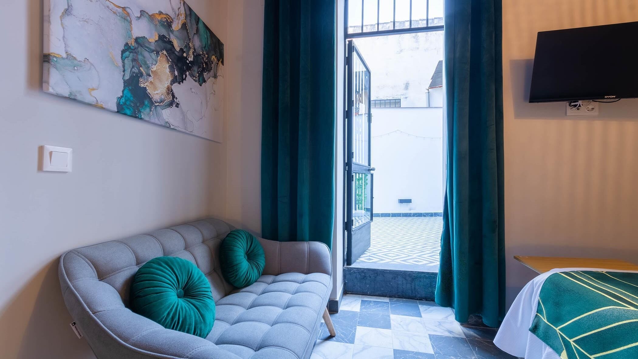A modern room with a grey sofa, teal cushions, a flat-screen TV, and a patterned floor.
