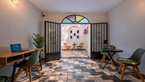 A modern interior with a checkered floor, a wooden desk with a laptop, two green chairs, a small round table with a plant, and a decorative wall with potted plants. - Zahra Center Cordoba ⭐⭐⭐⭐ (CORDOBA)