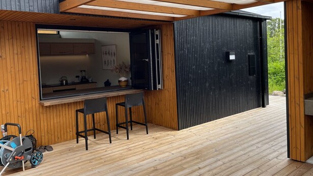 A modern outdoor kitchen area with a wooden deck, a bar counter, and two bar stools.