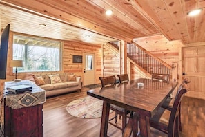 A wooden cabin interior with a dining table, sofa, and staircase. - Modern Luxury I Hot Tub I Hiking (McArthur)