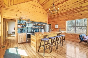 A wooden cabin interior with a kitchen, bar stools, and a large window. - Modern Luxury I Hot Tub I Hiking (McArthur)