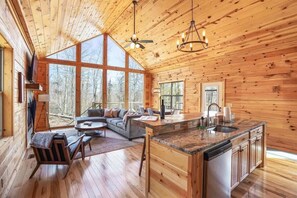 A spacious cabin with a large living area, a kitchen with a central island, and large windows offering views of the surrounding forest. - Modern Luxury Hocking Hills Cabin with Hot Tub (McArthur)