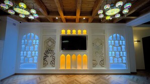 Una habitación con techo de madera, lámparas colgantes decorativas, un televisor de pantalla plana y diseños intrincados en las paredes.