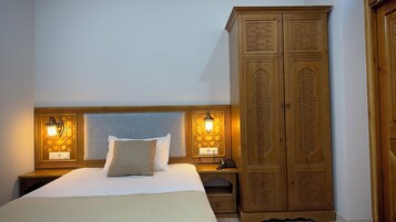 Una cama bien tendida con un cabecero, dos lámparas de noche y un armario de madera con intrincados grabados.