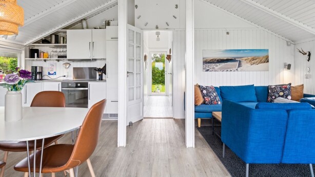 A modern kitchen with white cabinets, a dining area with a round table and chairs, and a blue sofa with patterned cushions.