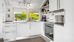 A modern kitchen with white cabinetry, a built-in oven, and a window overlooking greenery.