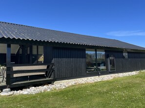 Un bâtiment doté d’un toit en métal ondulé, de grandes fenêtres et d’une terrasse en bois.