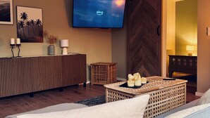 A modern living room with a flat-screen TV, a wooden console, a sofa, and a small table with candles.