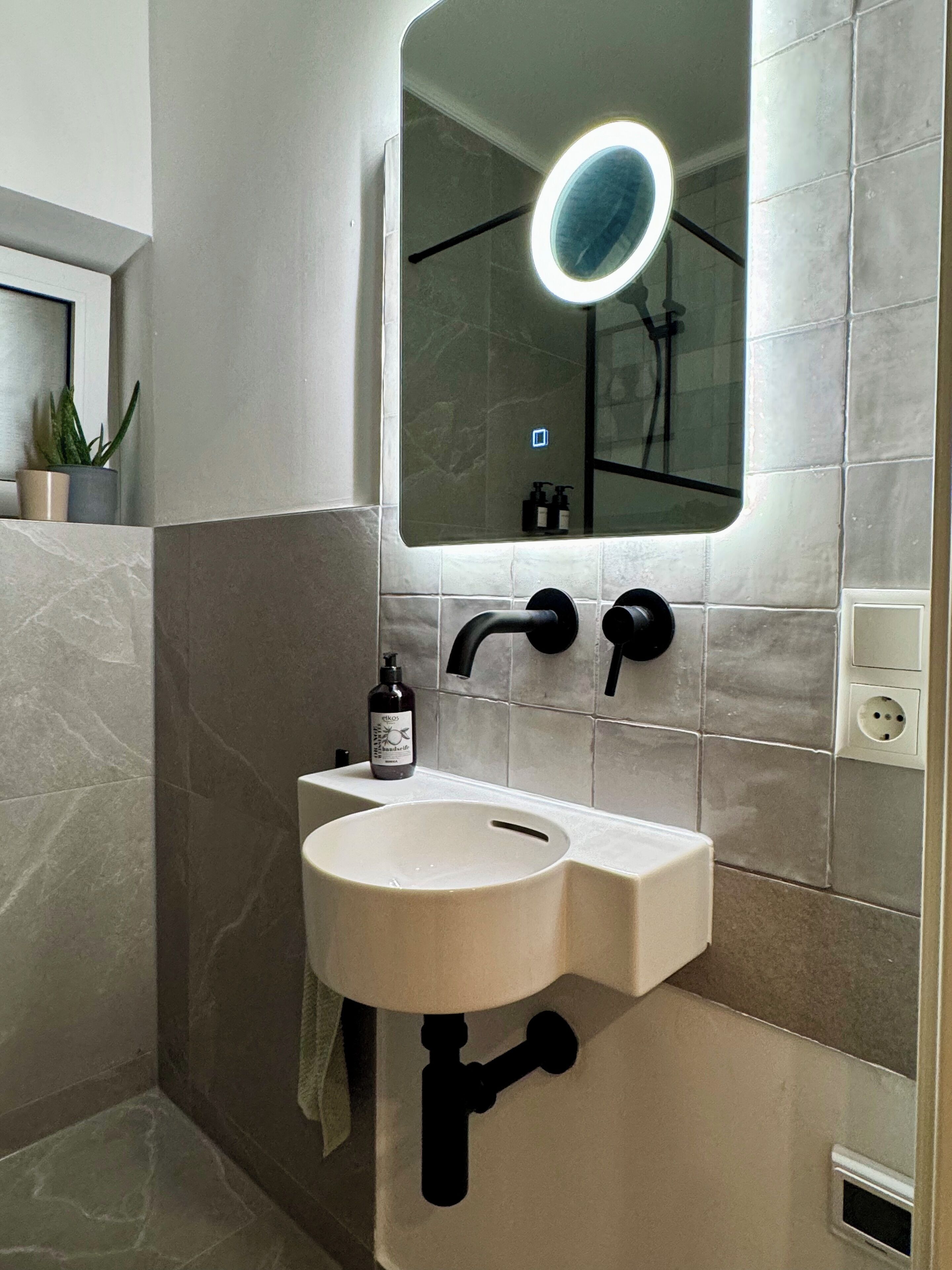 A bathroom with a white sink, black faucet, and a mirror with a light.