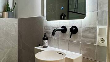 A bathroom with a white sink, black faucet, and a mirror with a light.