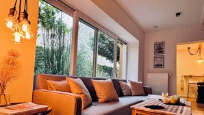 A modern living room with a sofa, a coffee table, and a view of greenery outside.