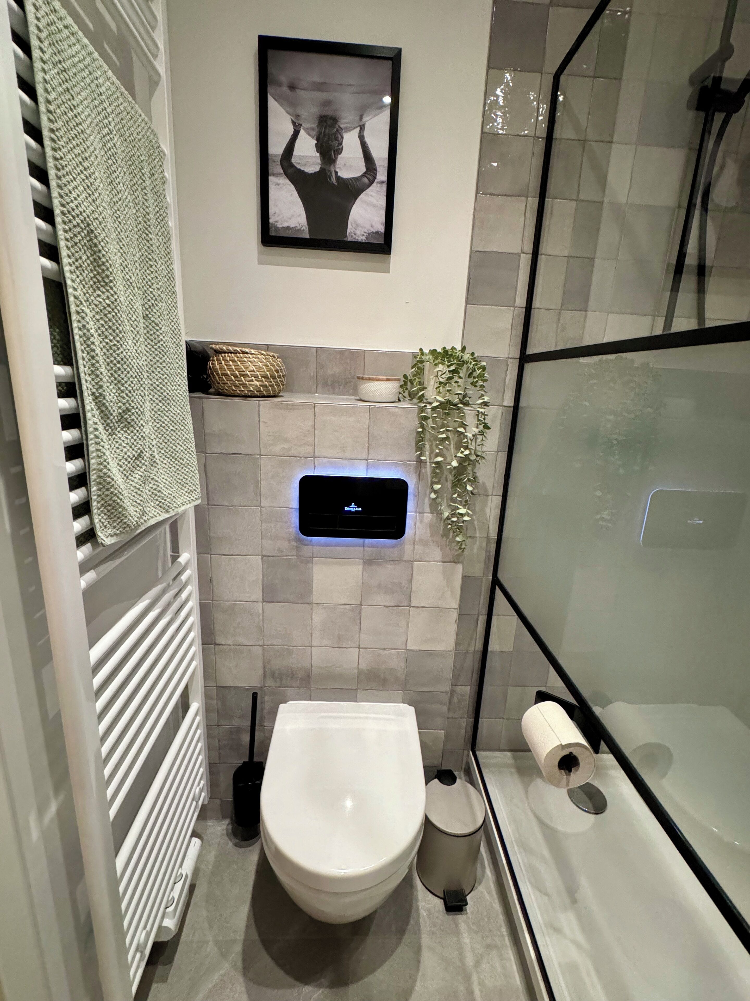 A modern bathroom with a toilet, bidet, towel rack, and a framed picture on the wall.
