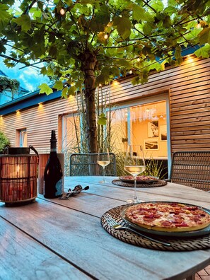 An outdoor dining area with a table set for two, featuring a pizza and wine glasses. - Gästehaus Grüne Oase - Im Zentrum von Minden (Minden)