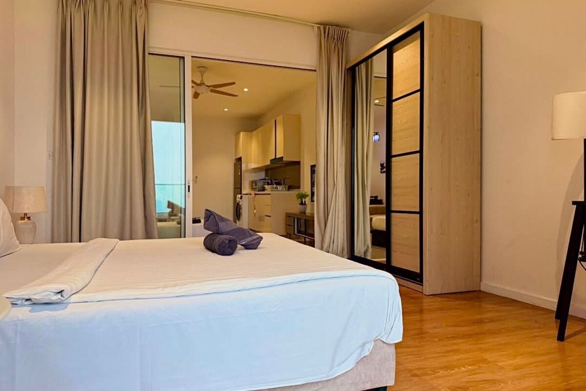 A bedroom with a bed, a ceiling fan, and a view into a kitchen area.